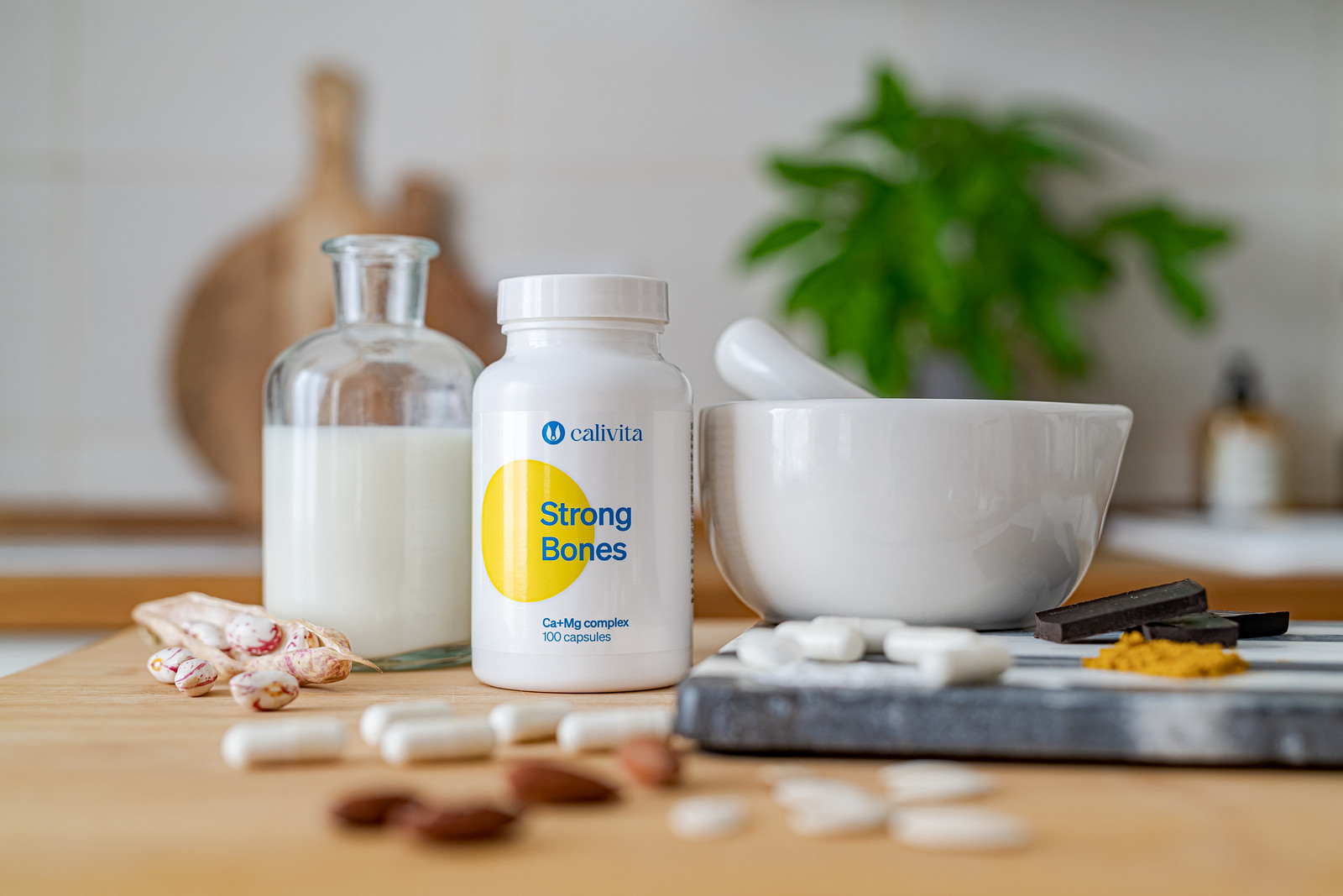 Flacon strong bones 100 capsule pe masa langa un mojar alb si o sticla de lapte